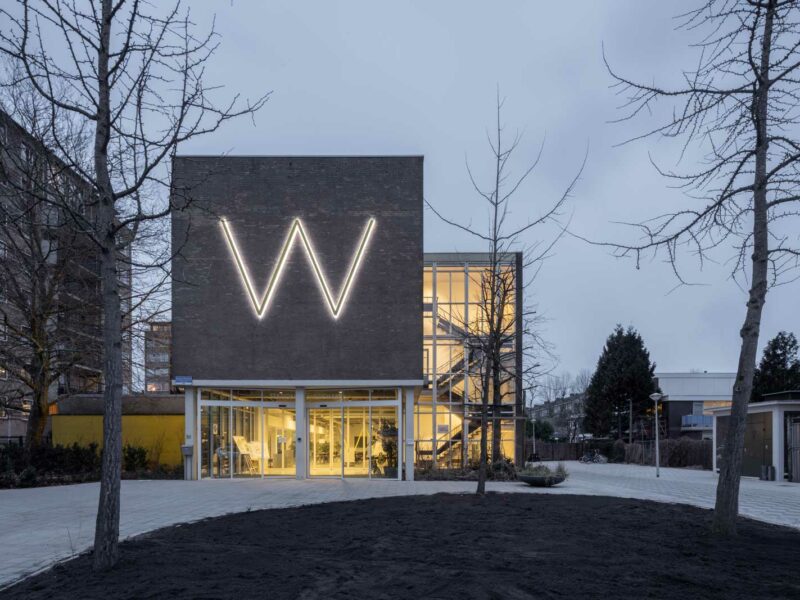 exterior evening photo showing prominent entrance and illuminated W on the front facade of Station Wildeman project in Amsterdam by beta evert klinkenberg auguste gus van oppen photo by Anna Odulinska